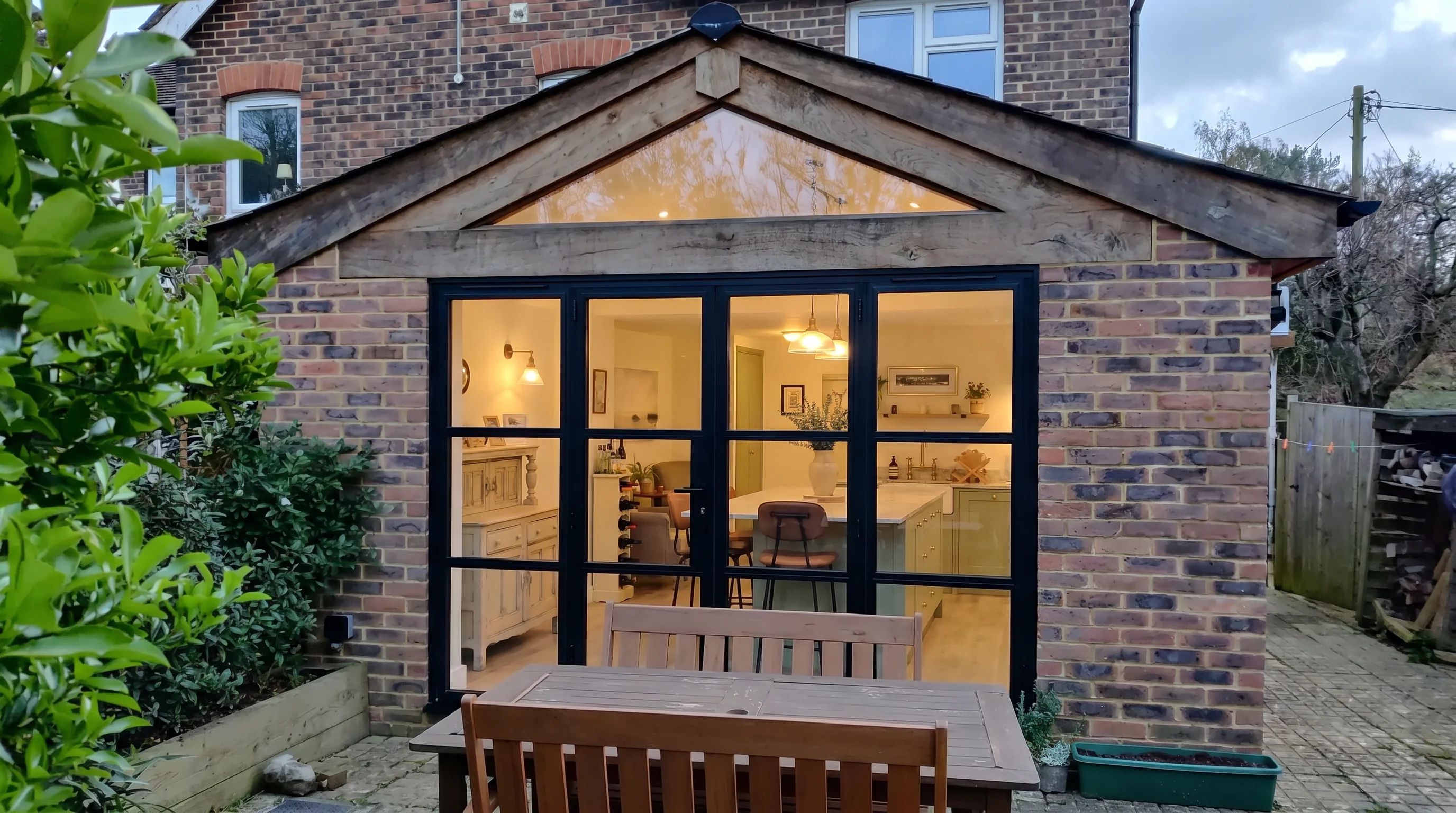 Rear elevation at dusk, oak-clad gable and steel-framed bifolds, Charlwood Surrey